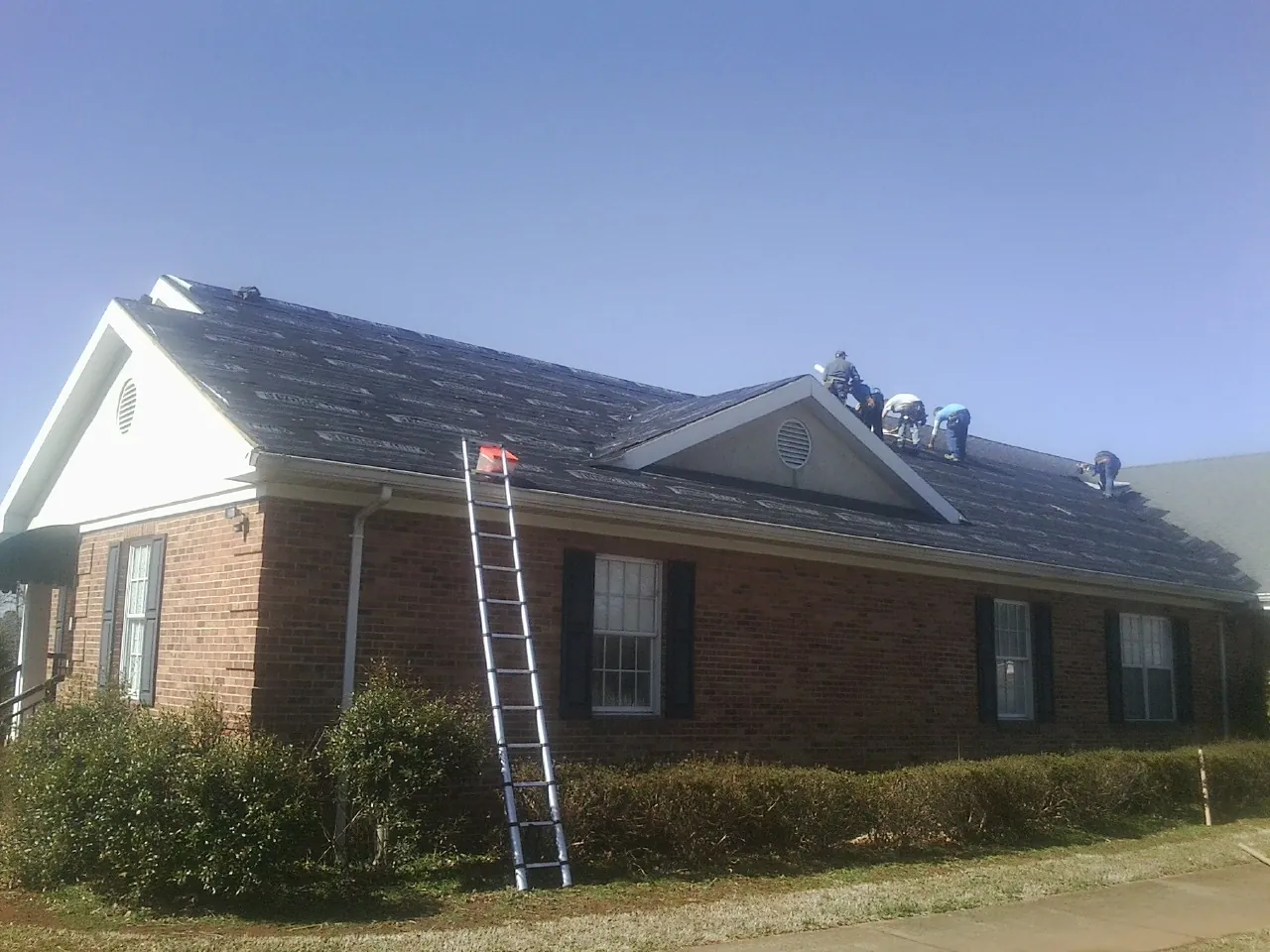 Crew tearing shingles off a brick ranch roof with a ladder set — Emergency Roof Repair work by our crew in Pekin