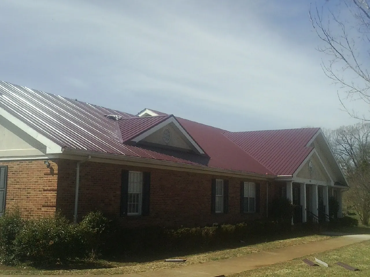 Red metal roof with gabled entries on a long brick building, from a Hail Damage Roof Repair job in Pekin