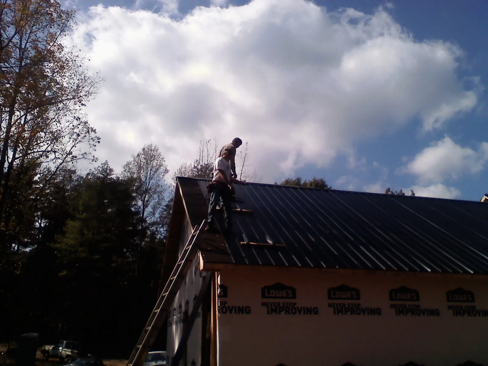 Roofer fastening dark metal panels high against a cloudy sky, from a Roof Inspection job in Pekin